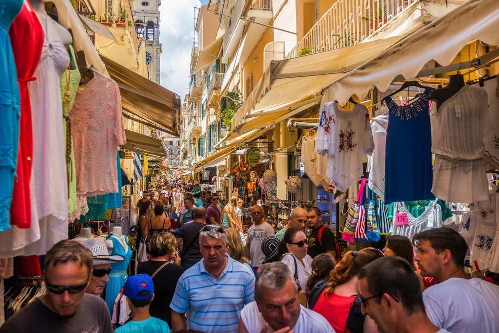 A crowded alley with various merchandise on each side are tourists are seen walking shoulder-to-shoulder. 