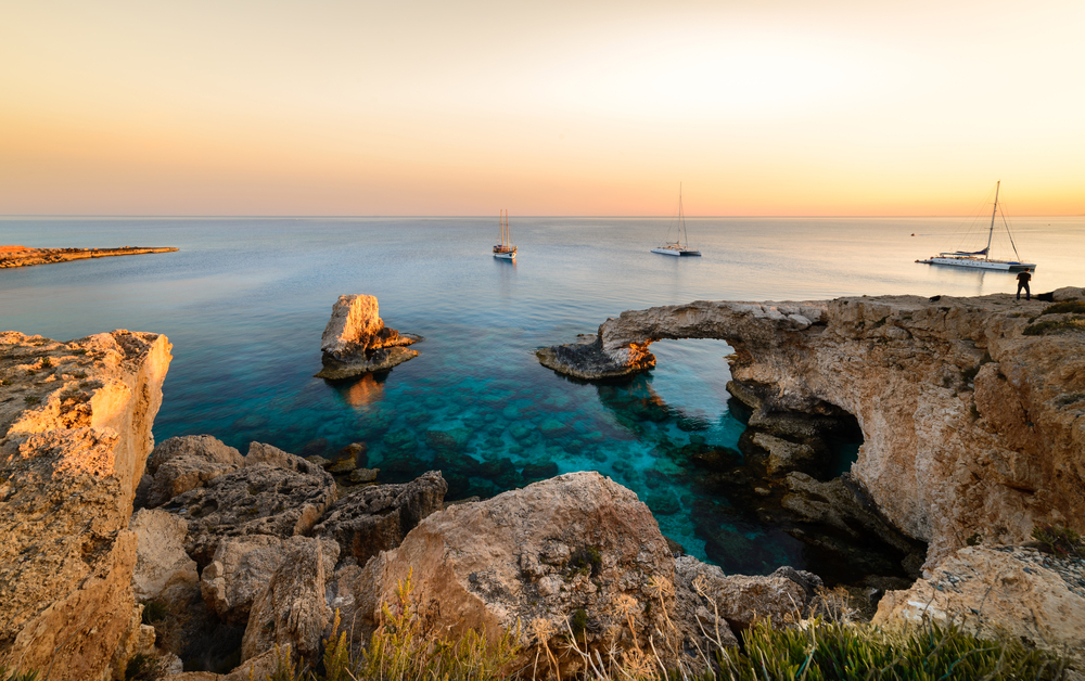 A sunset over a rocky coast with clear waters and three fishing boats. 