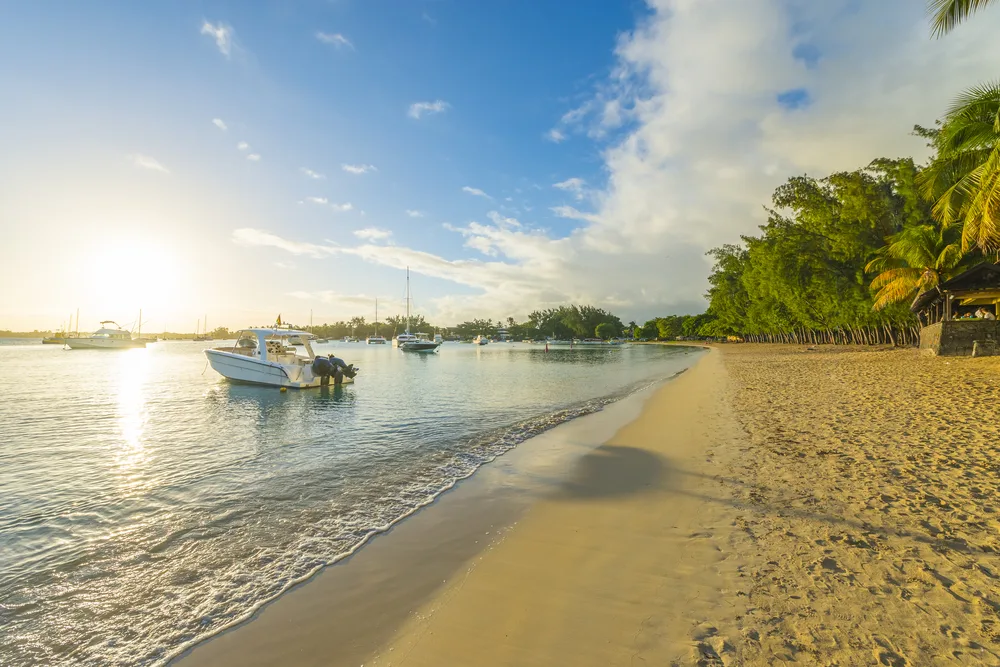 a sweet sunrise in Grand Baie, one of the best areas to stay in Mauritius, boats are moored near the shore with a treeline. 