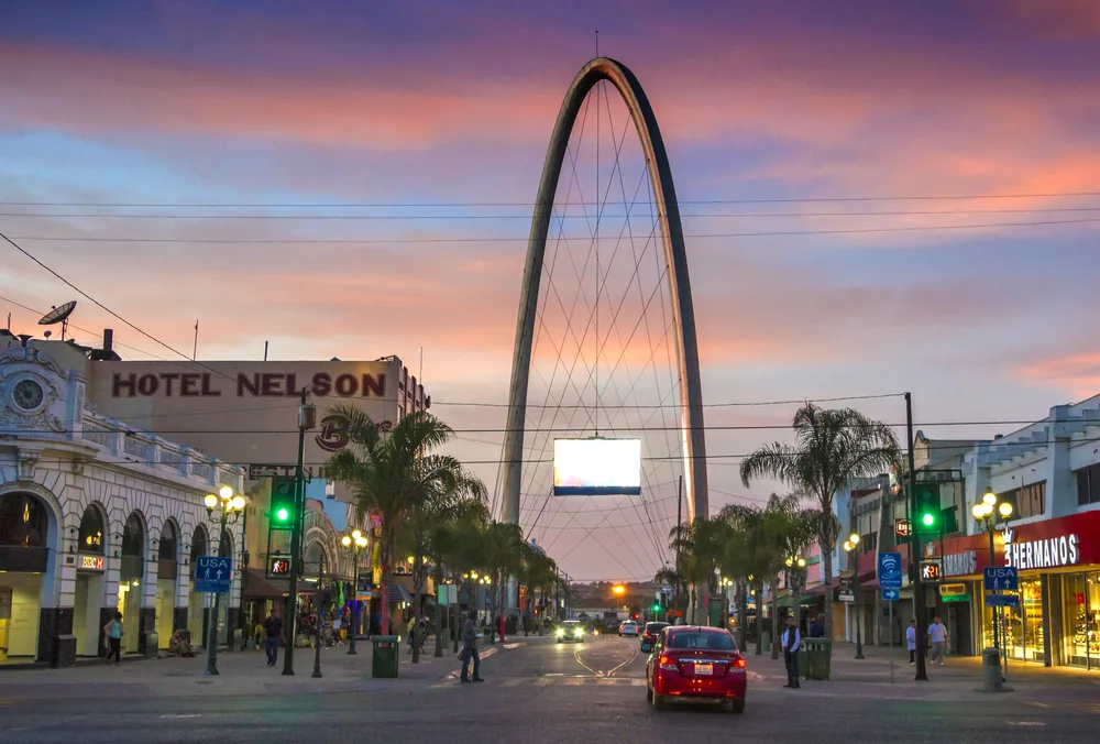 A gigantic arch structure can be seen at the middle of the street during a crimson sunset.
