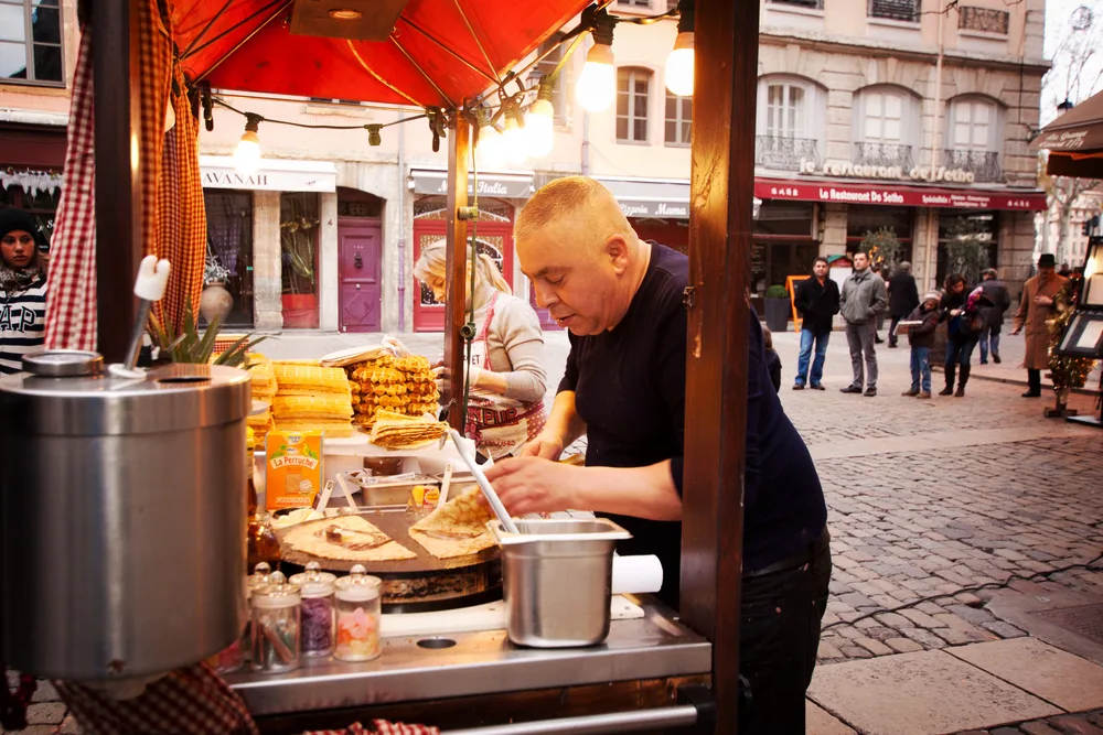 A vendor is preparing a pizza on his street food stall in Lyon during the overall best time to visit