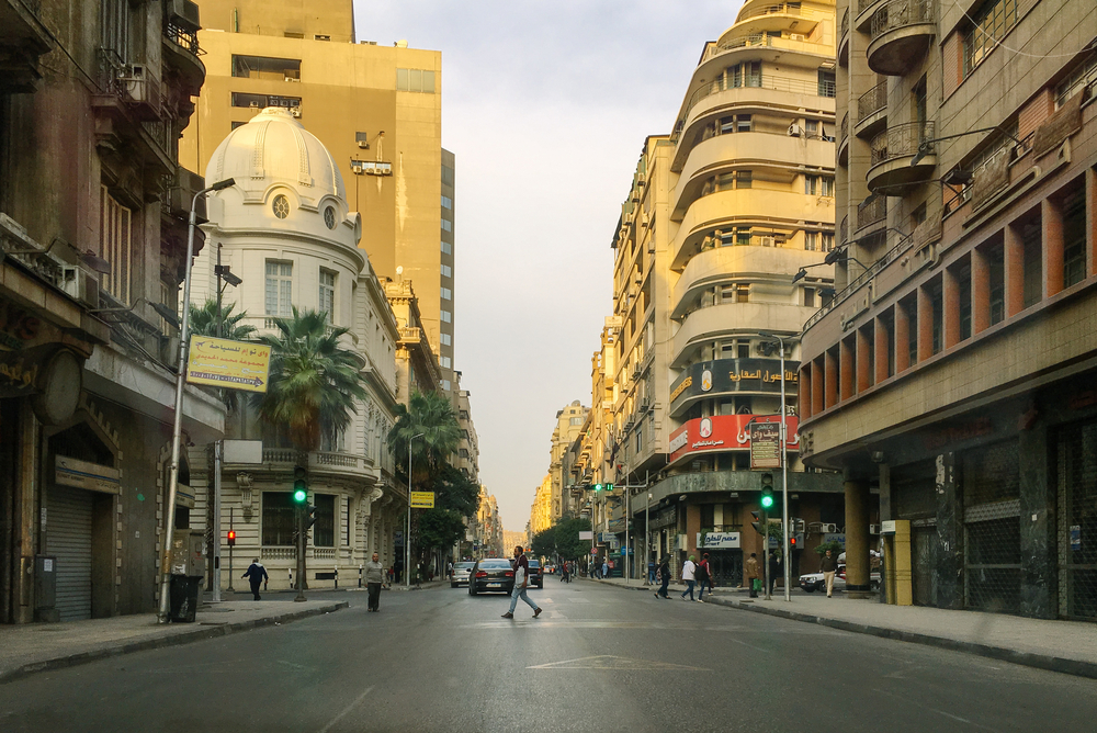 A person can be seen crossing a wide street in the Downtown, one of the best areas to stay in Cairo, with structures on both sides of the street.