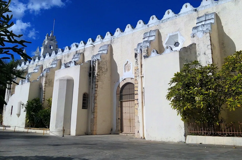 The old Parroquia de Santiago Apostol with its old peach paint sits below a clear sky in midday.