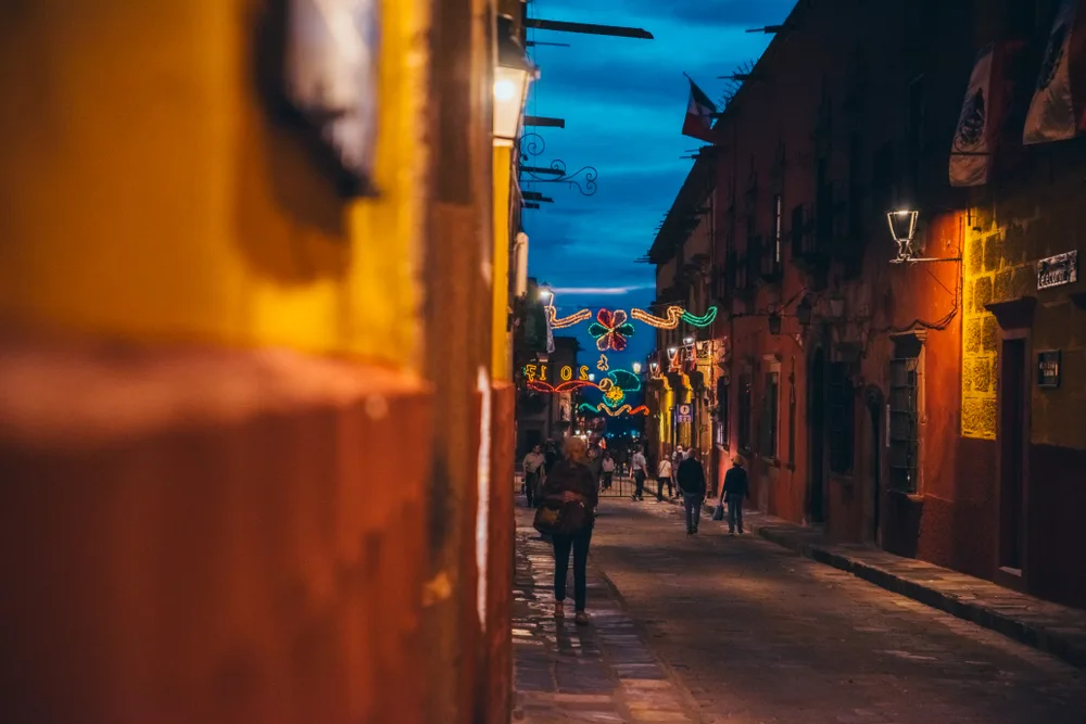 Several people walking down an alley illuminated the street lamps at dusk in Guadalpue, a top pick for where to stay in San Miguel