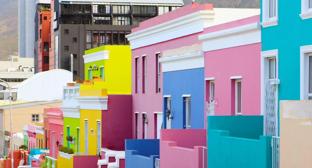A row of pastel colored houses in Bo-Kaap, one of the best places to stay in Cape Town, and a modern building in background. 