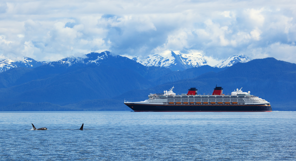 Beautiful shot of an Alaskan cruise ship with 2 orca whales breaching the water and mountain scenery in the background for a list of the best all-inclusive vacations no passport needed