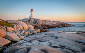 A lighthouse located at a rocky coast with calm sea during a sunset.