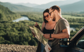 A couple stopped on the roadside in the mountains smiling with a map in hand for a list of the best weekend trips in the US