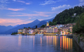 View of a lake town during dusk where the lights are reflected on the lake and some mountains can be seen in background.