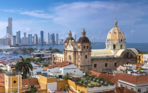 Aerial view of a town where in the foreground is an old church together with other structures and in background is another island with tall and modern structures.