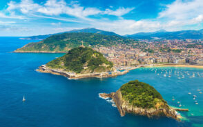 Aerial view of an island with a city near its coast, where some portions of the island and mountains and trees, and in the coasts, boats are visible near the shore.