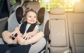 A toddler placed in a car seat smiling while enjoying the ride during sunset.