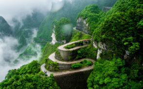 A winding road built on the side of a mountain covered with trees where it is fogging.