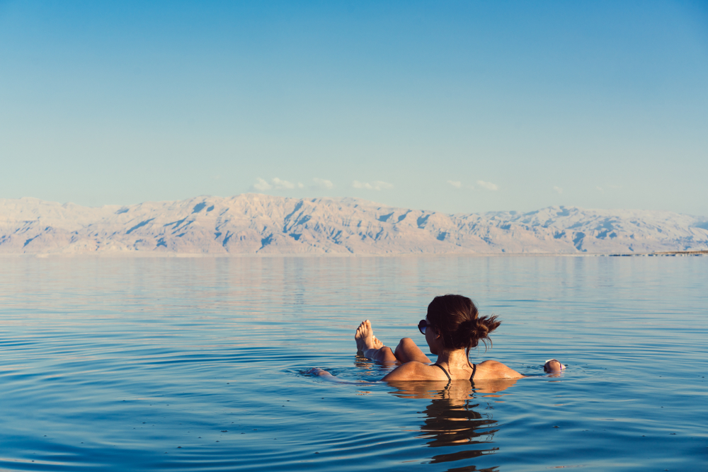 A woman can be seen floating in a seating position on a sea and mountains can be seen in background. 