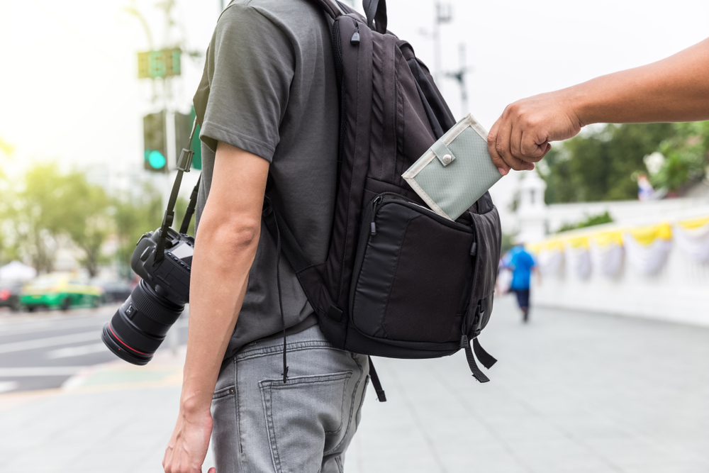 A pickpocket stealing a wallet from the bag behind a tourist with a camera dangling from his neck. 