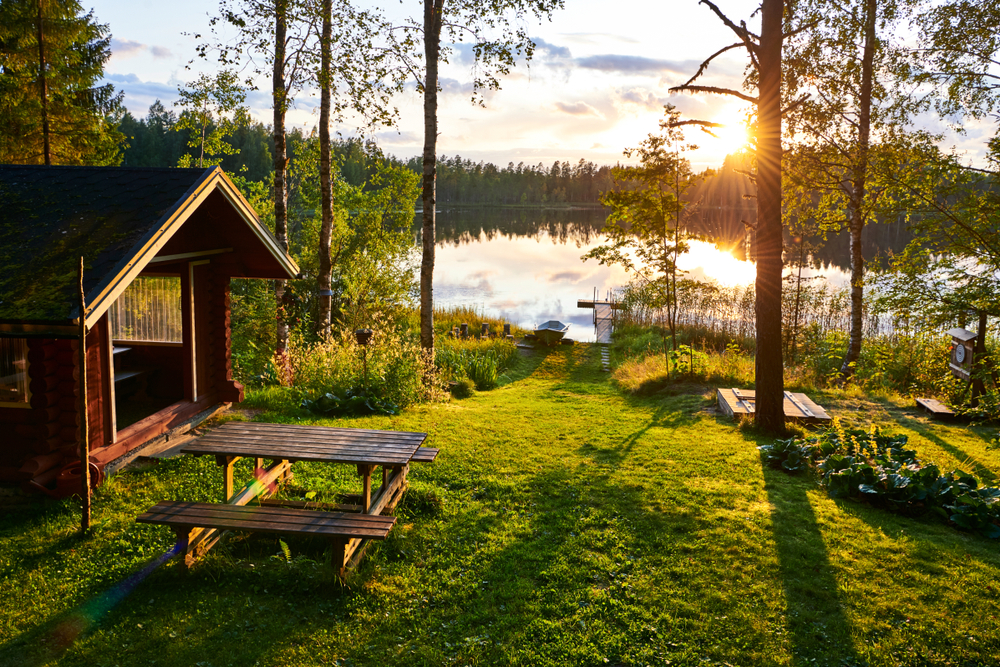 A cabin by the lake surrounded by trees during a sunset. 
