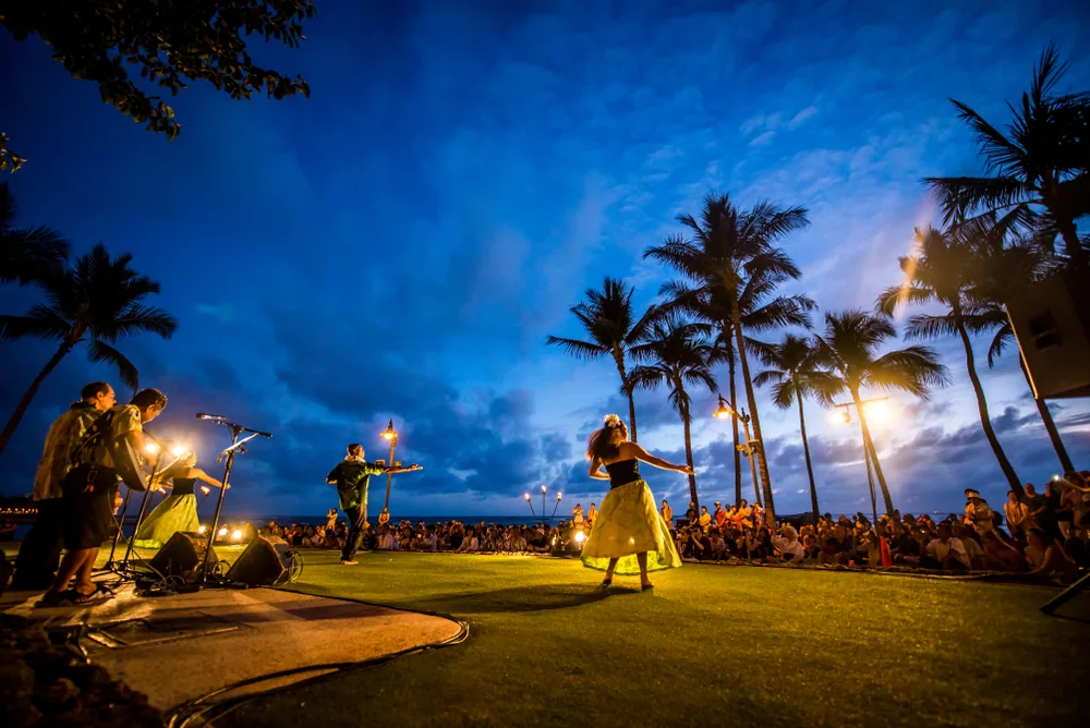 Concept of what language do they speak in Hawaii represented with a nighttime view of a traditional Hawaiian luau with a hula dancer and band performing