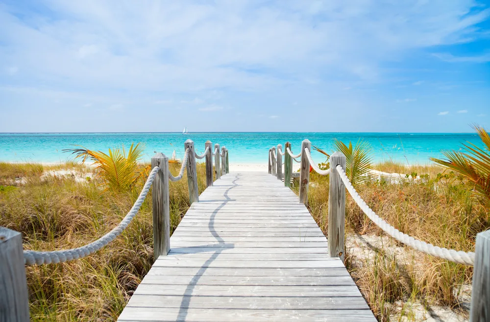 View down a wooden walkway leading to the beach on Providenciales island for a guide explaining how long a direct flight to Turks and Caicos takes on average