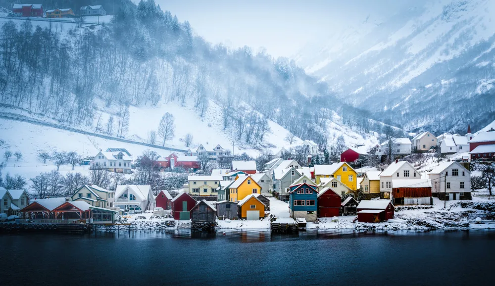 Houses on the valley near the sea are covered with snow, and mountains with bare trees and mists, an image that implies hard weather conditions and safety in visiting Scandinavia.