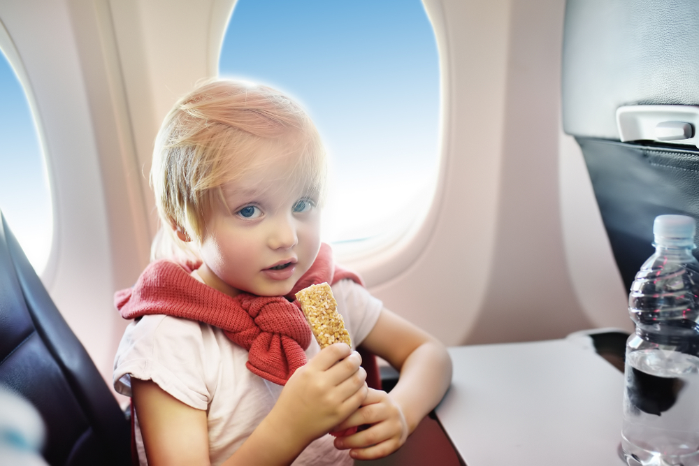 Blonde child holds a granola bar with both hands during a flight for a guide answering the question can you bring snacks on a plane?