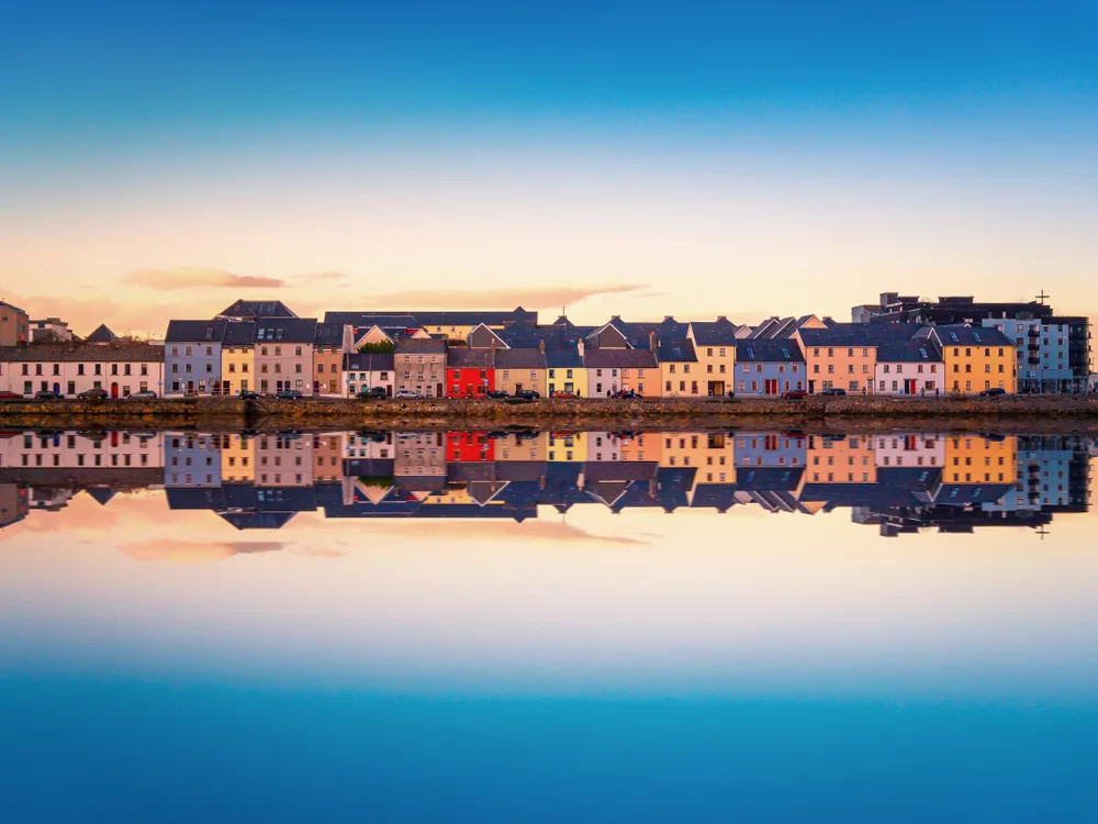 Paste colored houses can be seen reflected on still water during sunset.