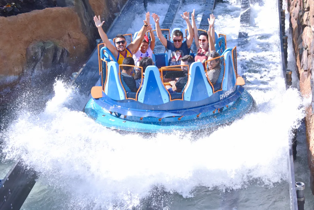 A group of people raising their hands in excitement as the are riding a water ride in a theme park. 