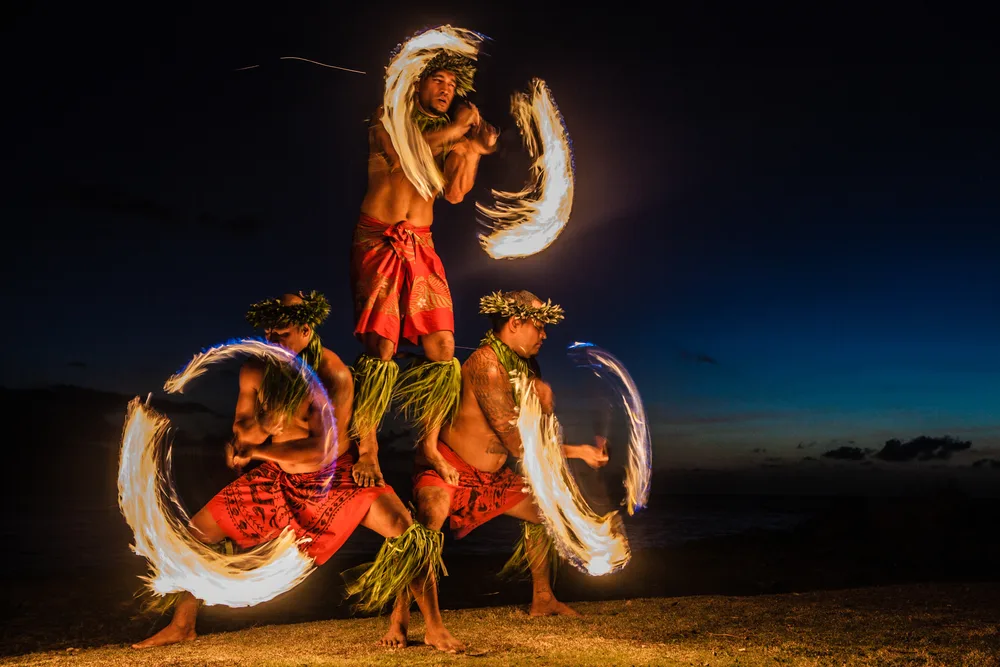 Three men juggle fire batons during a nighttime luau celebration in Hawaii for a piece discussing what language do they speak in Hawaii?