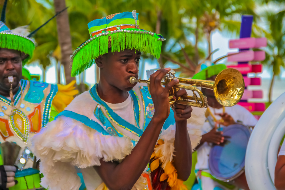A local blowing a small trumpet while wearing a tasseled hat during a festival. 