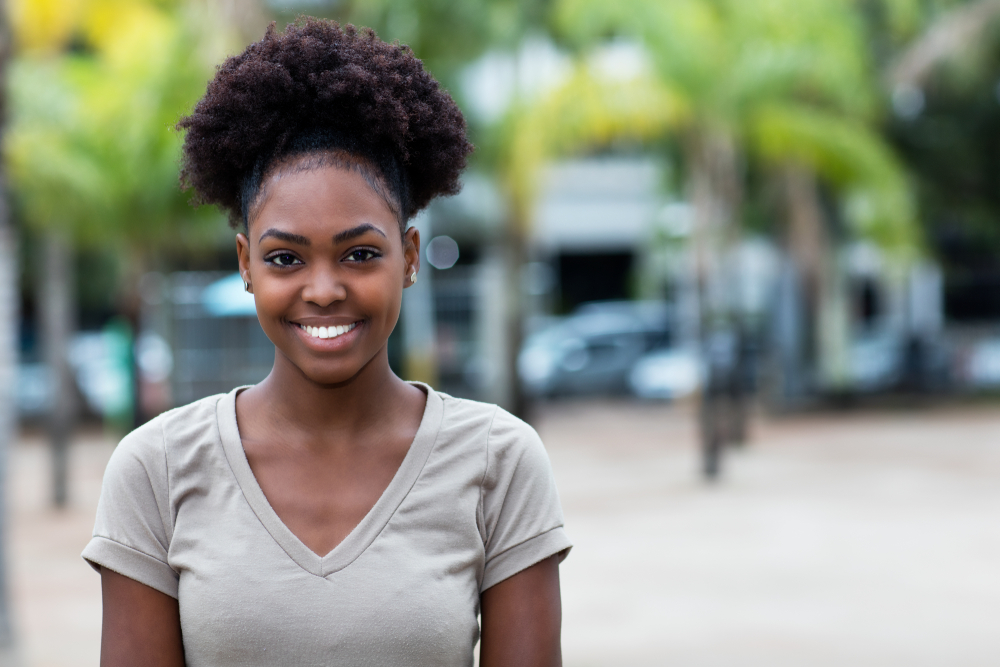 A Caribbean woman wearing a grey shirt smiling for the camera.