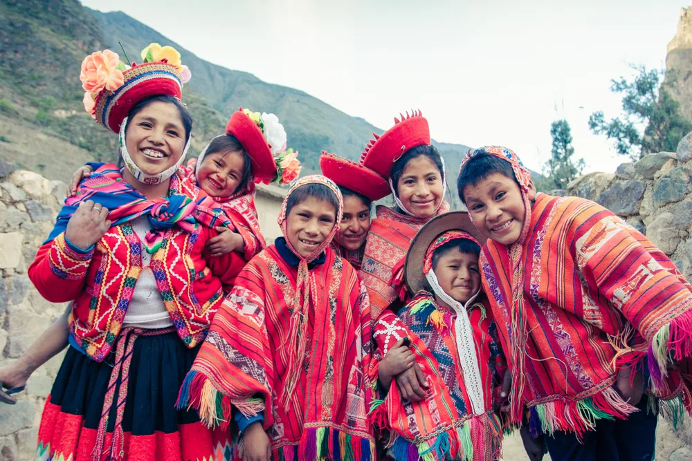 Latin American local kids wearing traditional woven clothes in red color with blue accent, smiling for the camera, an image for a piece on the list on facts about Peru.