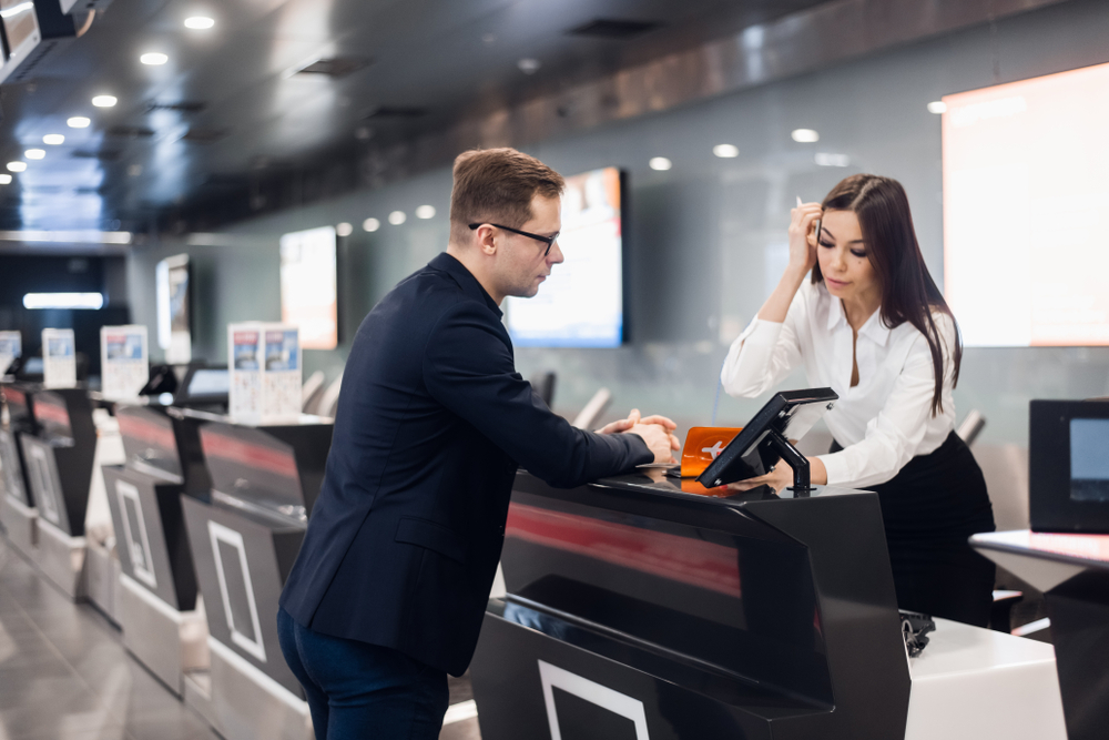 Businessman at the airport check-in counter talks with a female agent about how much it costs to fly standby