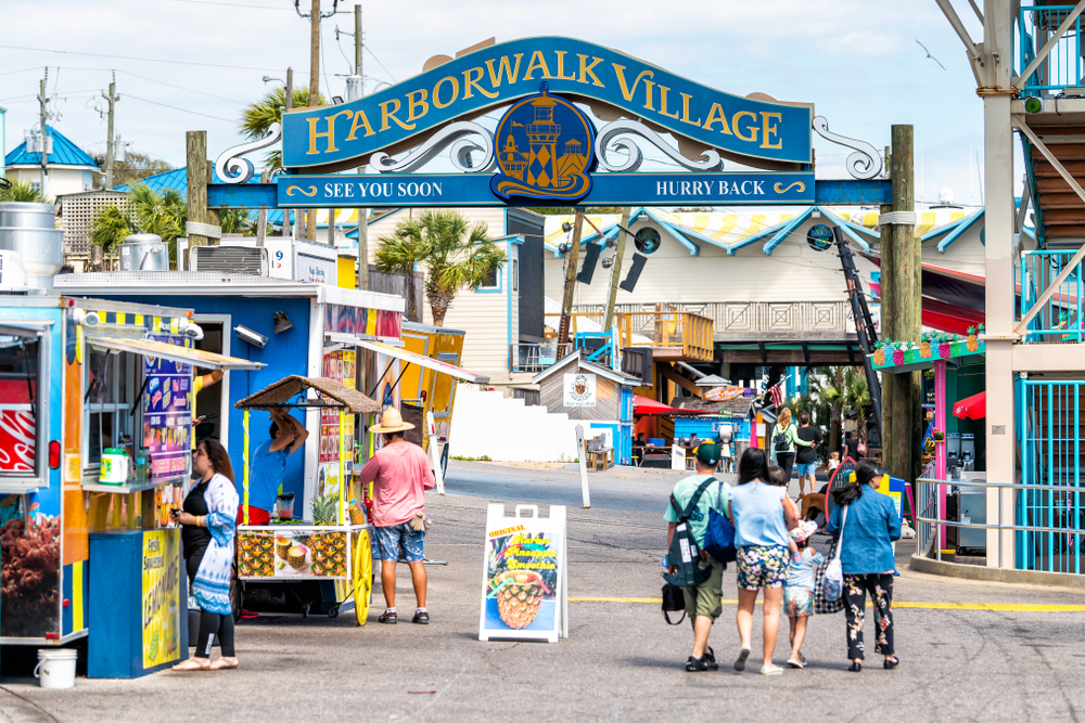 A small area that has an arch sign of "Harborwalk Village" with small stores, and a family can be seen exiting. 