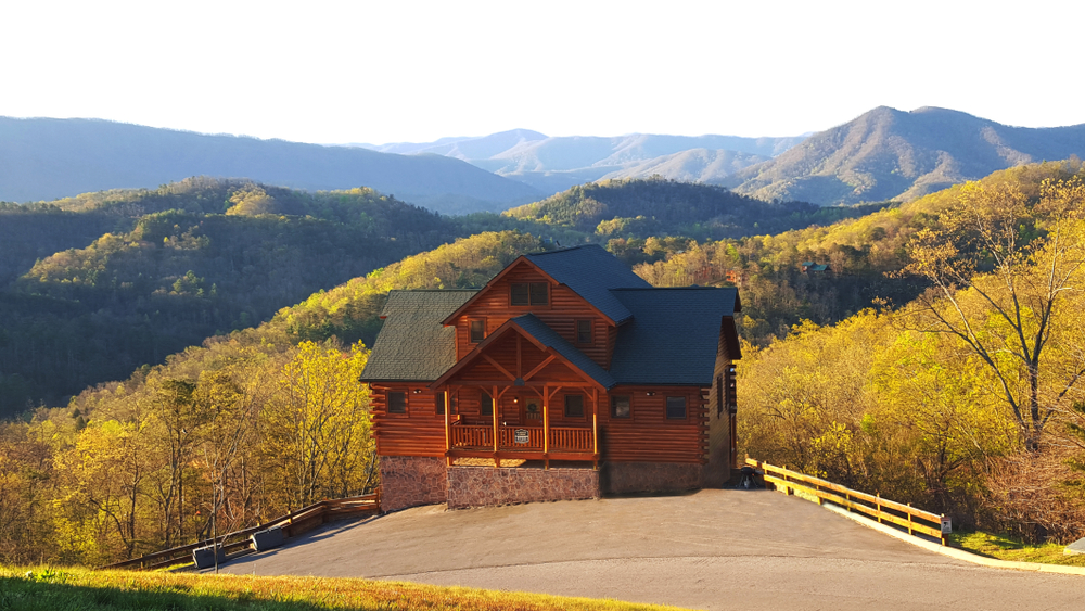 A lonely cabin on a mountain surrounded by trees during autumn, with a view of mountains with lush forest, an image for a travel guide about trip cost to Gatlinburg. 