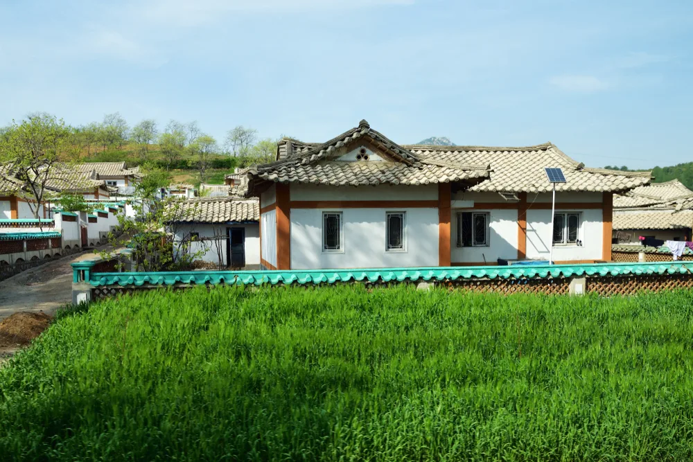 An old house with tile roofs can be seen with a small solar panel, and in front of the house is a grass area.