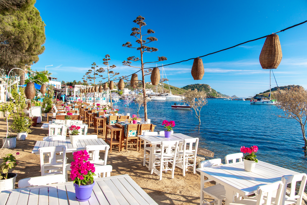 A view of a restaurant beside the coast with white chairs and table and hanging native ornaments. 