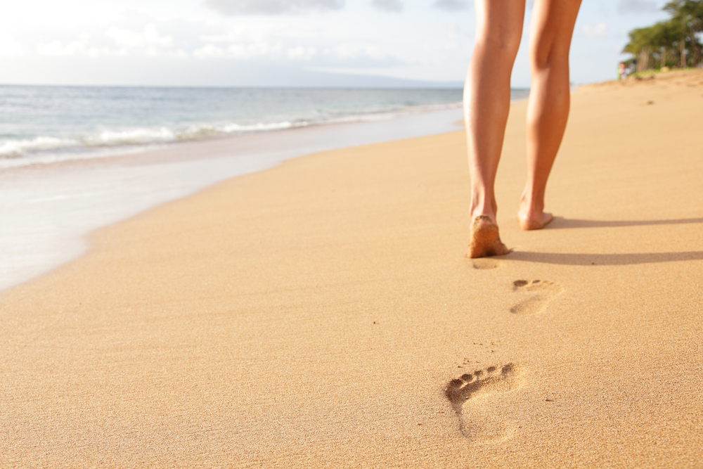 A woman walking on the shore leaving footprints on the sand.