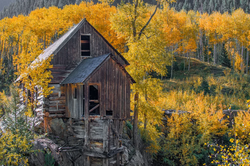 An old cabin on a rock surrounded by trees during the autumn season.