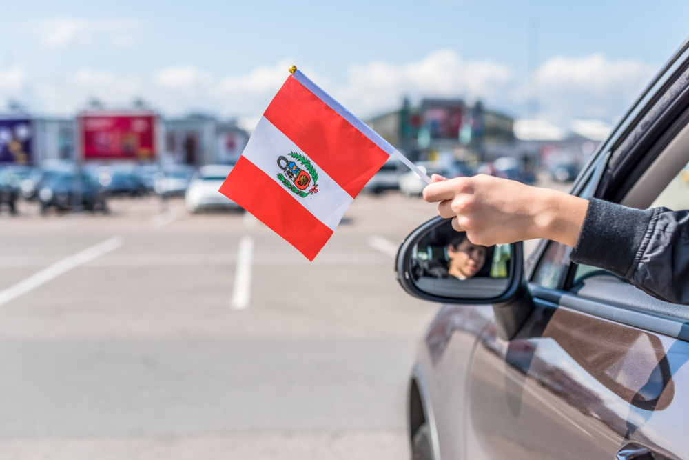 A person holding a Peru flag out of a car window while parked.