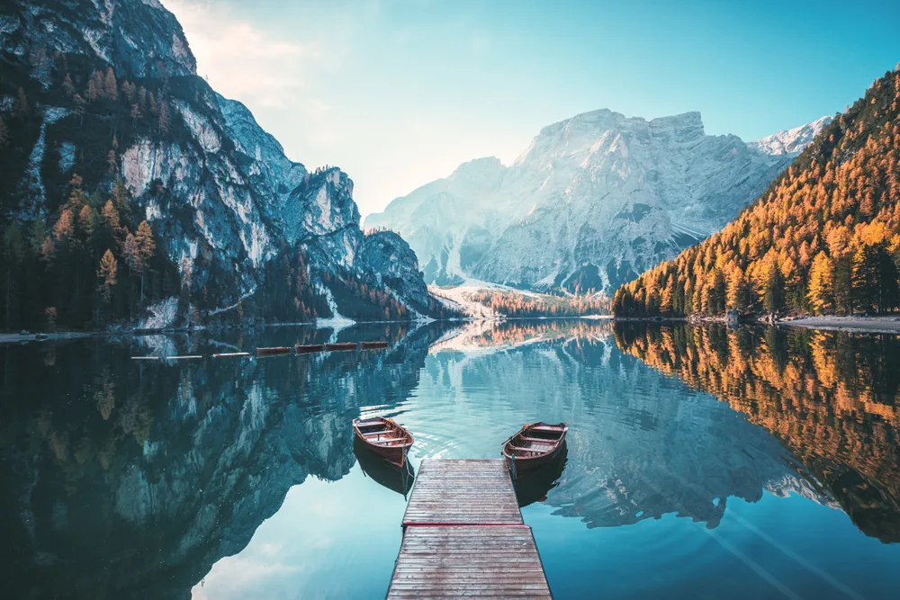 Two boats on both side of the dock, for a piece on where to stay in the Italian Lakes, a still lake reflecting the cold mountains and trees during an early morning.
