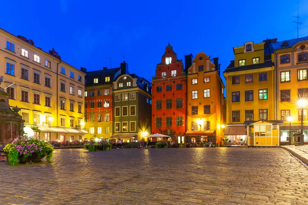 An empty town square paved with bricks illuminated by street lights in an evening, an image for a travel guide about trip cost to Scandinavia.