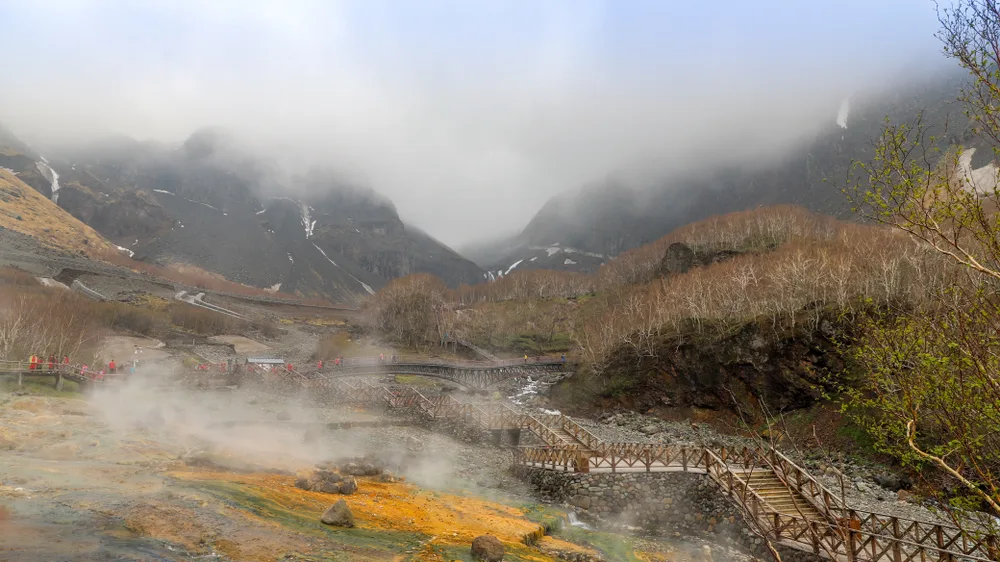 An early morning in a hot spring where a mountain can be see covered with fog and steam can be seen from the ground. 