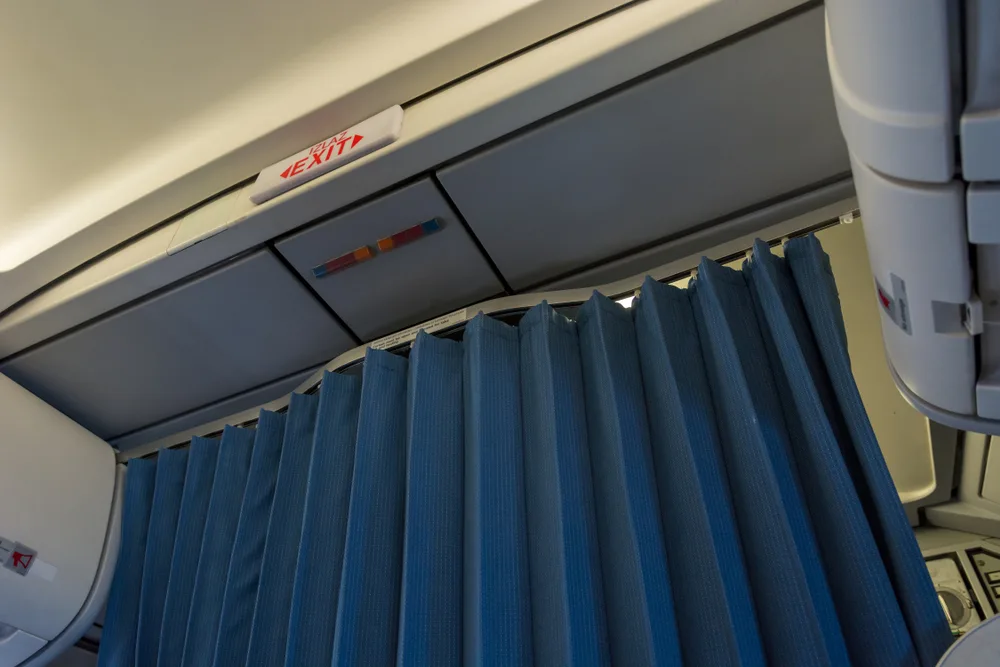 What is a bulkhead can be answered with imagery of a blue curtain partition "wall" or bulkhead in a plane, shown with Exit signage as seen from the first row