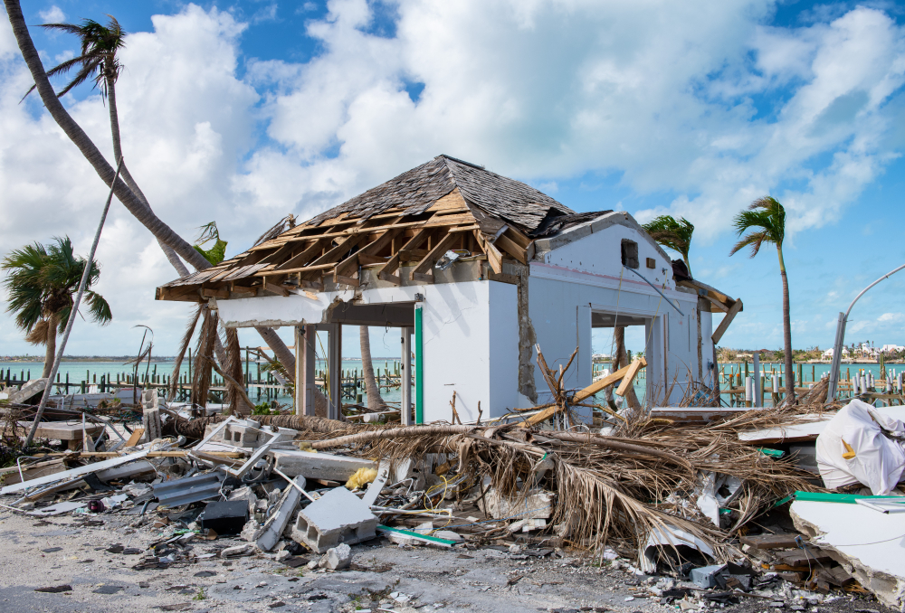 A destroyed house and broken palm trees in the coastal area after a typhoon, a piece on the guide titled when is the hurricane season in the Bahamas.