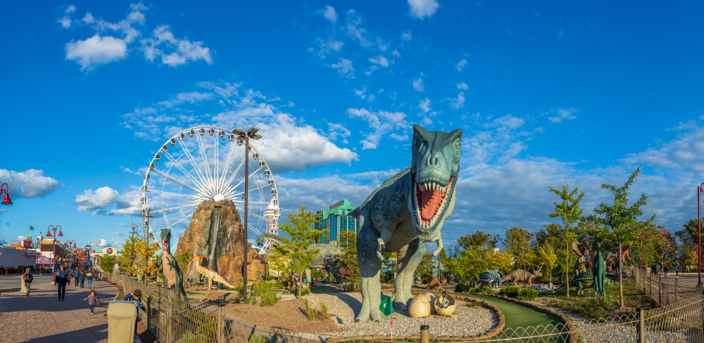 An amusement park with a large ferris wheel and a huge t-rex statue.