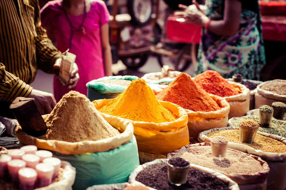 Spices displayed on a market place in sacks to the brim, with measuring cups placed above each sack, a section image in an article about trip cost to Morocco.