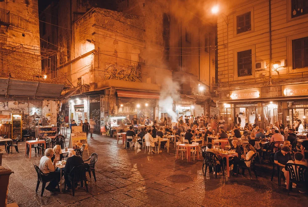 Many people eating outdoors in front of a restaurant during a calm evening.