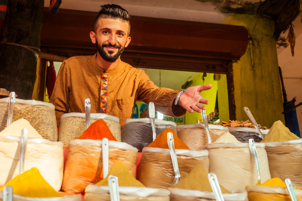 A local store vendors selling spices can be seen gesturing to check his merchandise while smiling. 