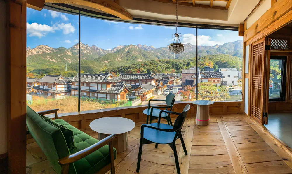A hotel room with wooden floor and accents has a wide glass window what has an overlooking view of the mountains. 