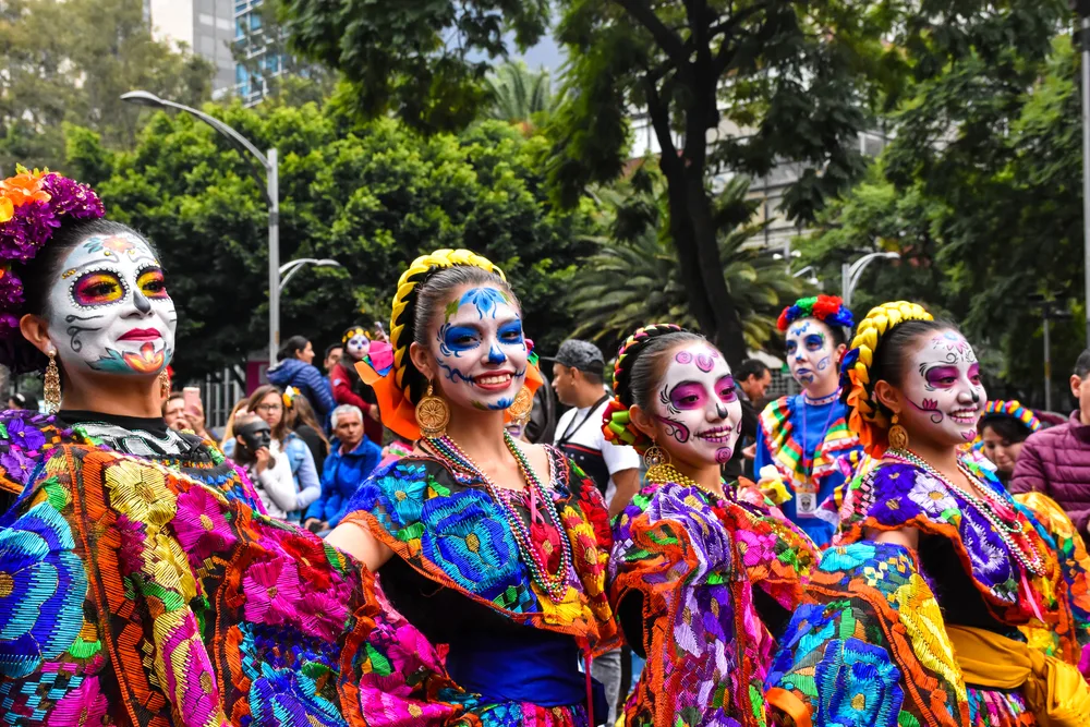 Women with their faces painted while wearing vibrant festival clothing during a local celebration during the least busy time to visit Acapulco.