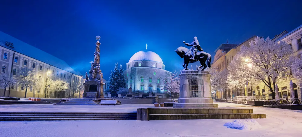 A town square during winter where a man riding a statue can be seen and a mosque.